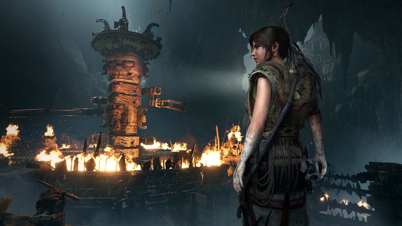 Shadow of the Tomb Raider에서 라라 크로프트가 마야 조각상 모닥불 앞에 서 있습니다.